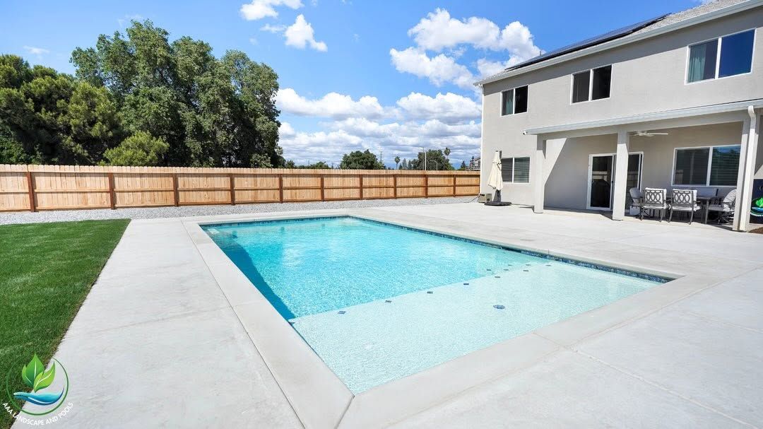 Backyard swimming pool beside a two-story house on a sunny day