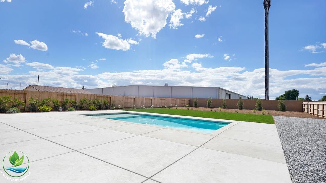 Backyard patio with a small in-ground pool, concrete deck, gravel border, and blue sky