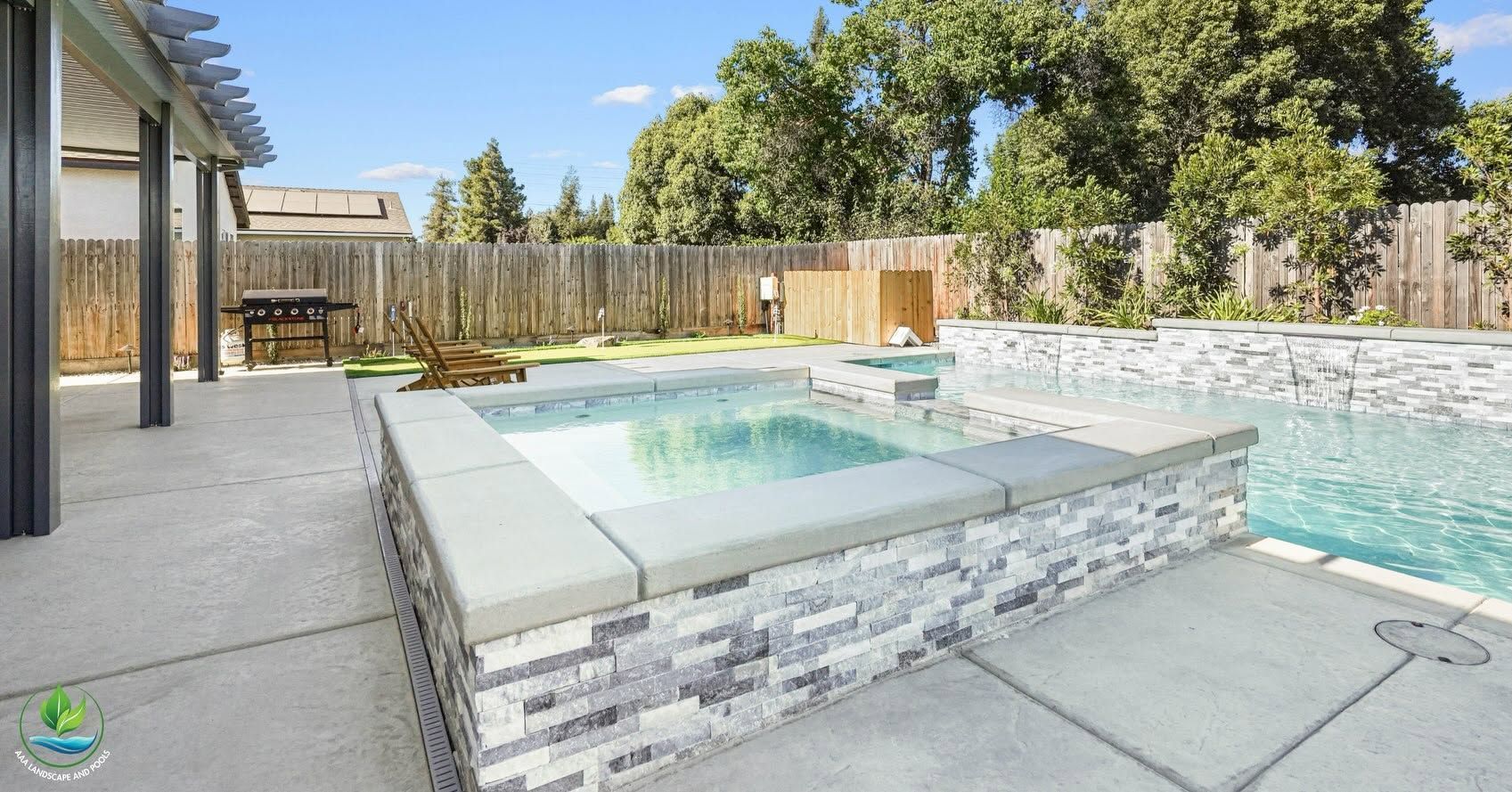 Backyard patio with a raised hot tub beside a turquoise swimming pool under a clear blue sky
