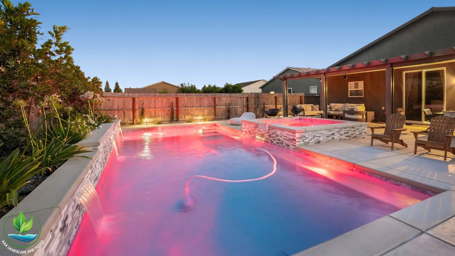 Backyard swimming pool glowing pink at dusk beside a patio and house
