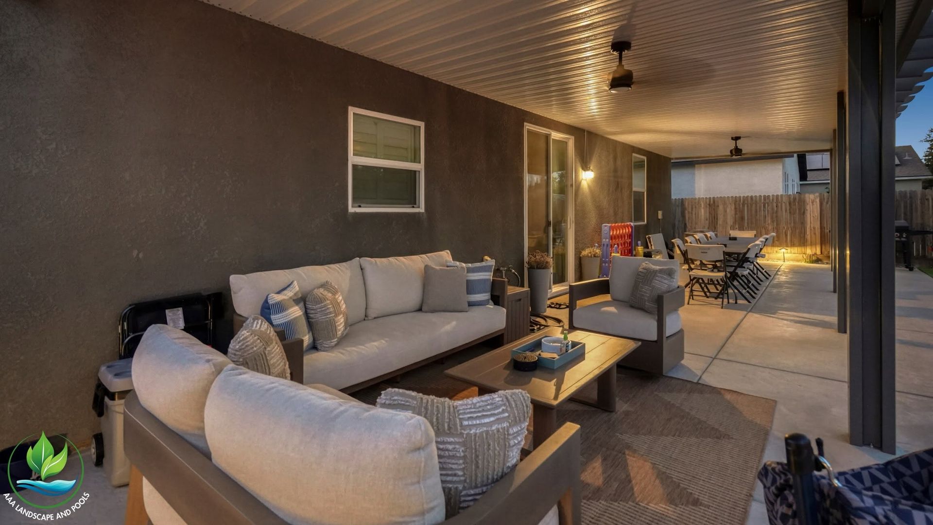 Covered patio with gray sofas, coffee table, and dining set at sunset.