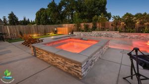 Backyard patio with a sunken stone fire pit glowing orange at dusk, surrounded by trees and a fence