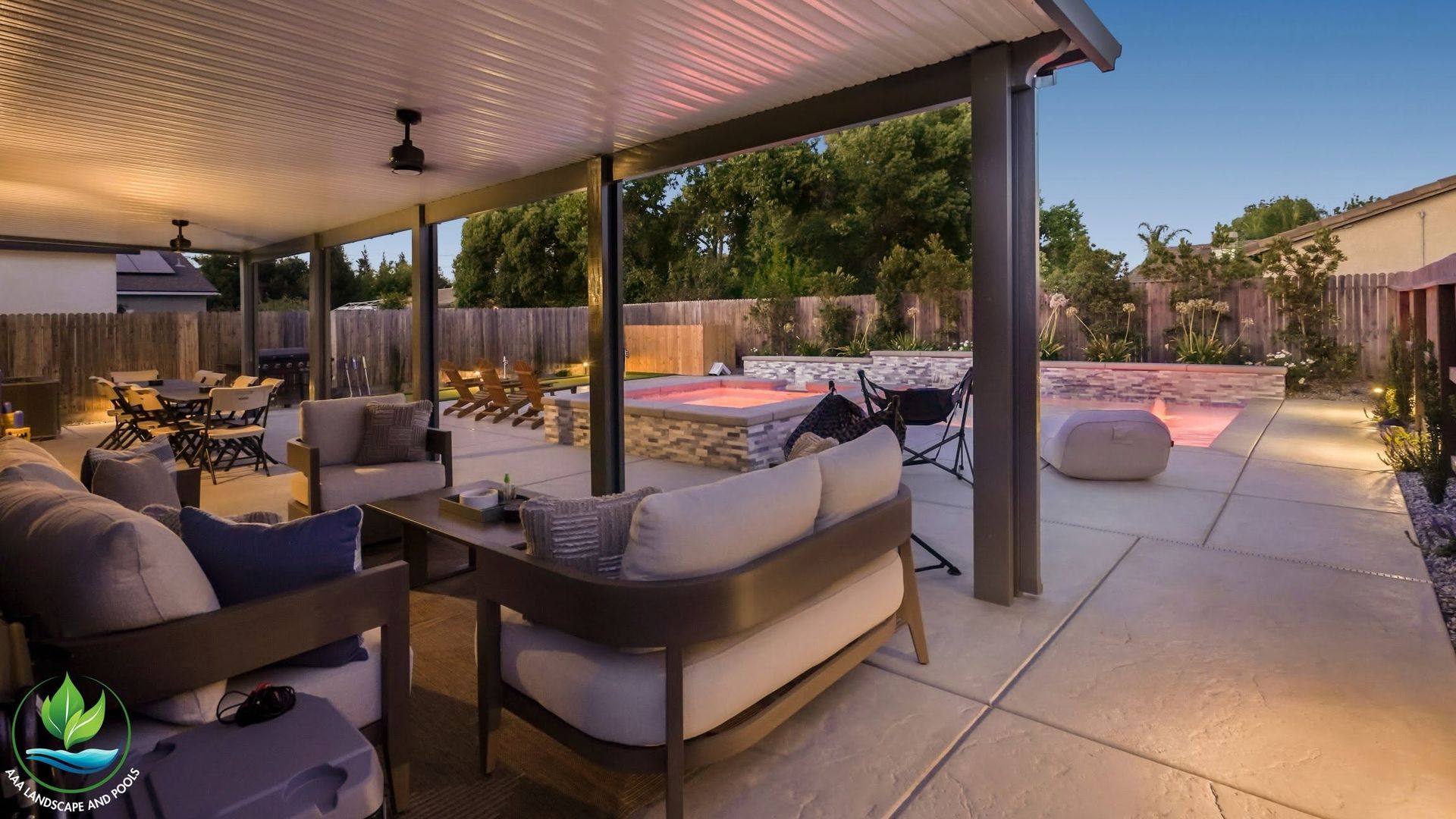 Covered patio seating overlooking a lit backyard pool at dusk