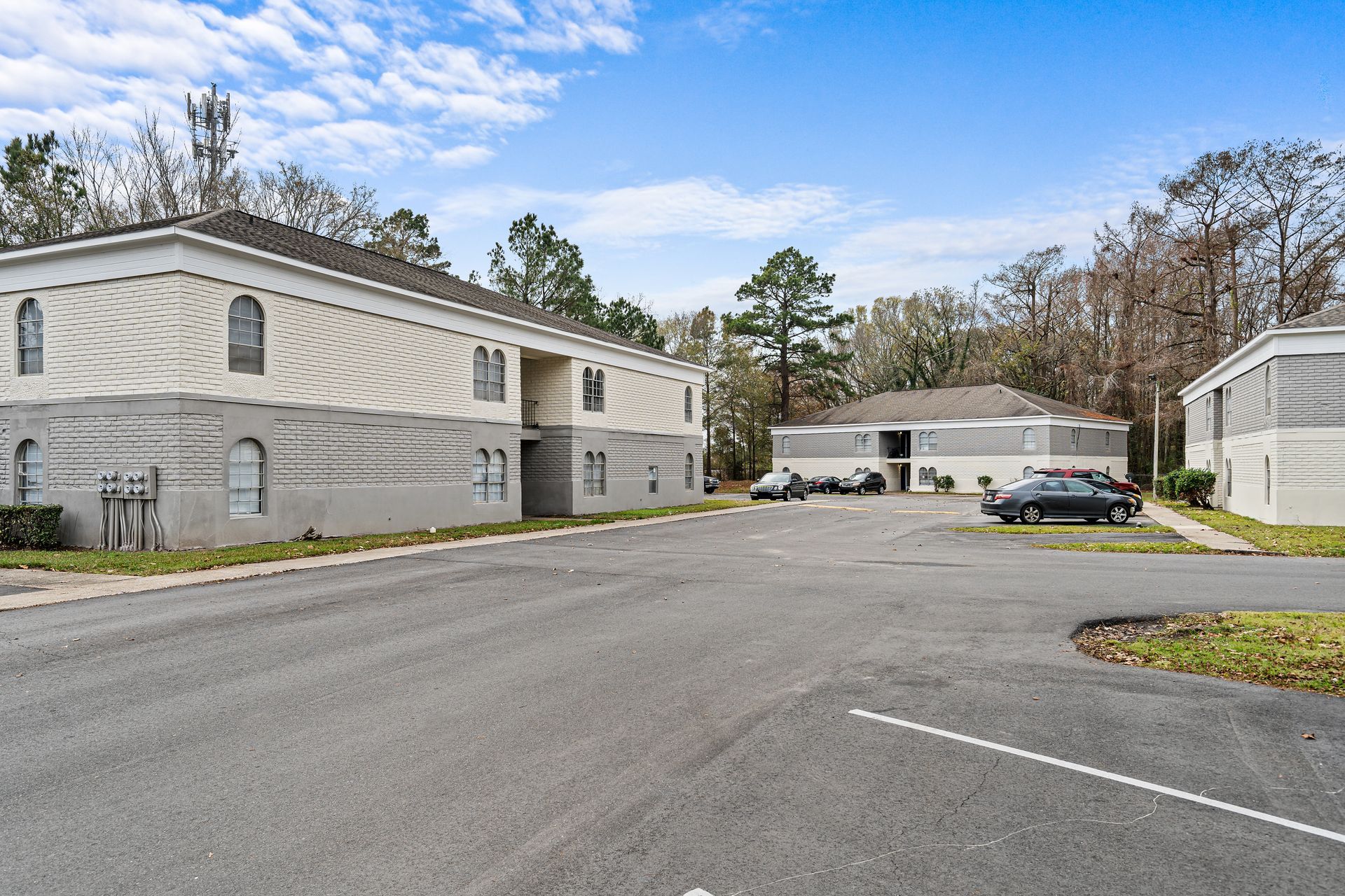Apartment complex parking lot with gray buildings, parked cars, and a partly cloudy sky