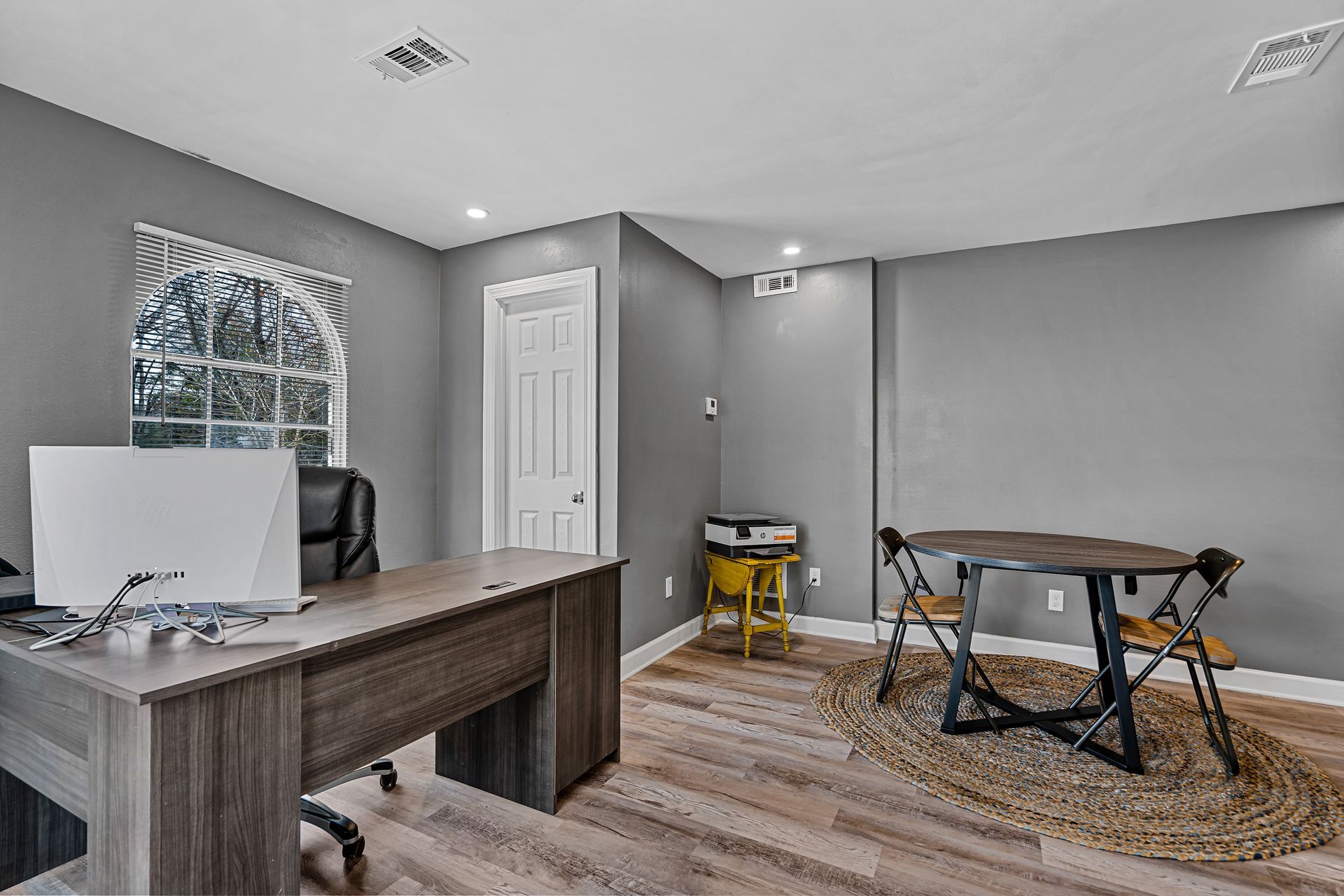 Home office with desk, computer, gray walls, and a small workbench on wood flooring