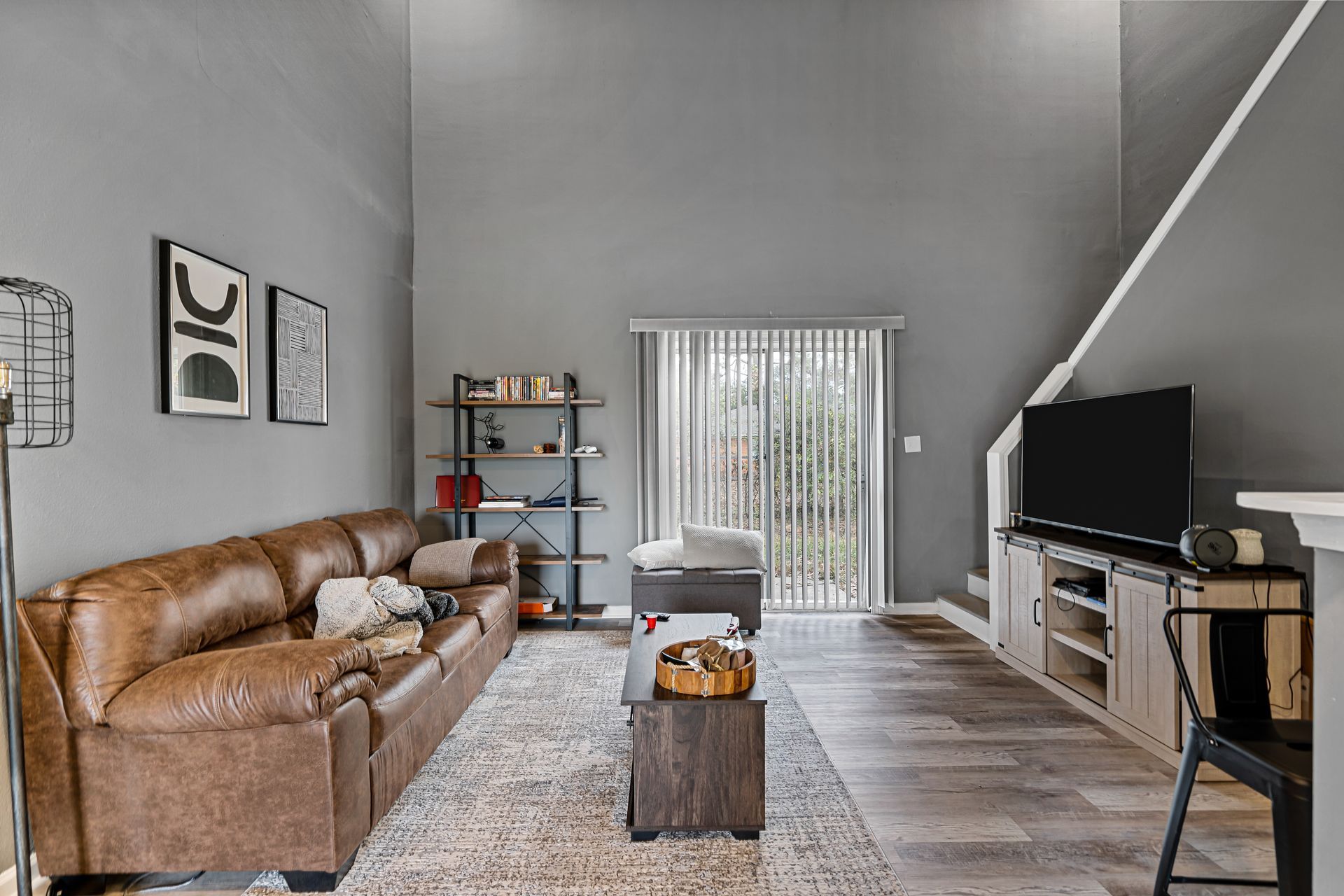Modern living room with brown sofa, gray walls, TV, rug, and sliding glass doors to a patio