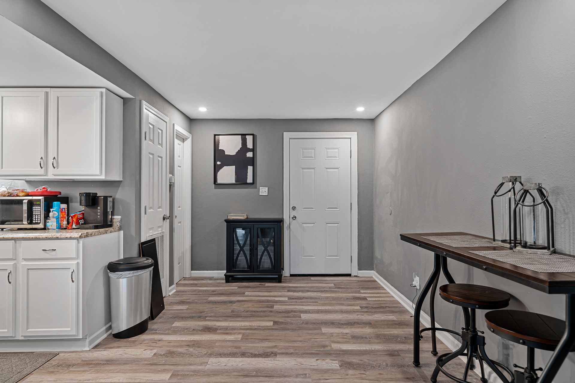 Bright hallway with white cabinets, wood flooring, a small table, and a closed door.