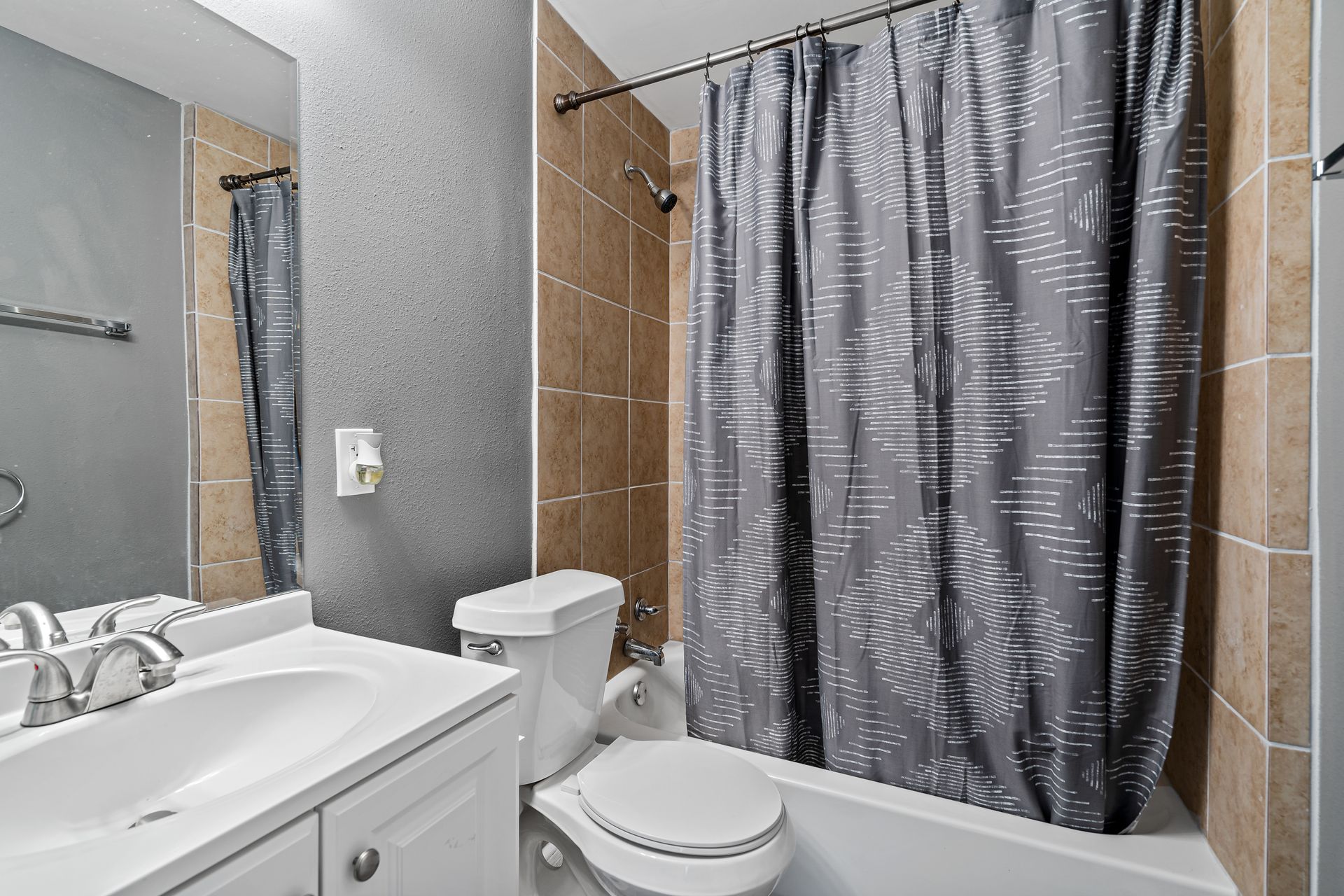 Small bathroom with white vanity, toilet, tub, and gray shower curtain.