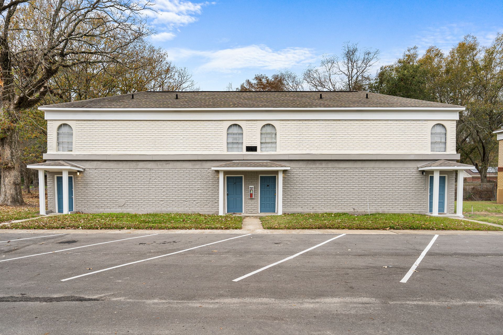 Empty parking lot in front of a two-story beige building with a blue door and windows