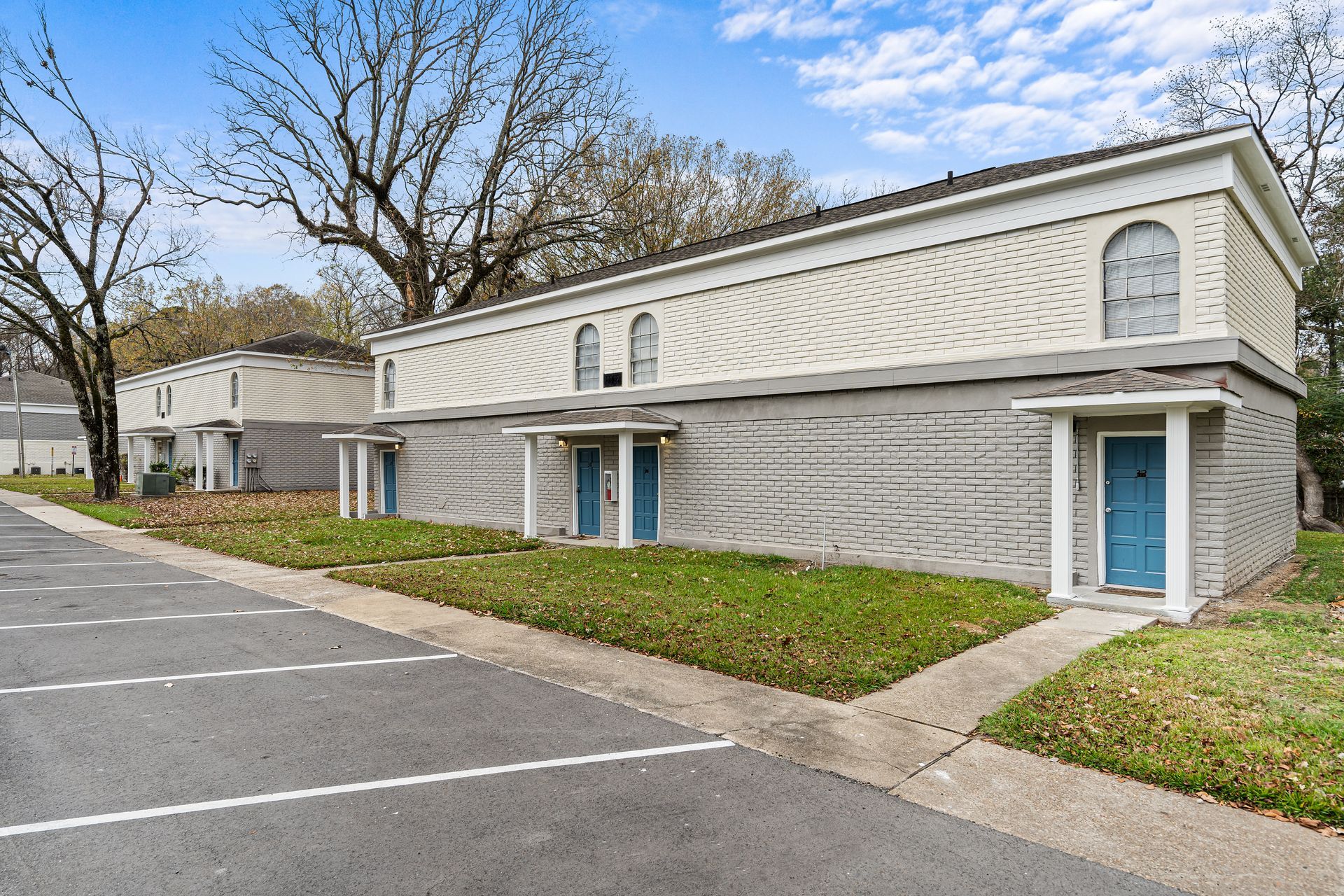 Exterior of a gray apartment building with blue doors and parking lot in front
