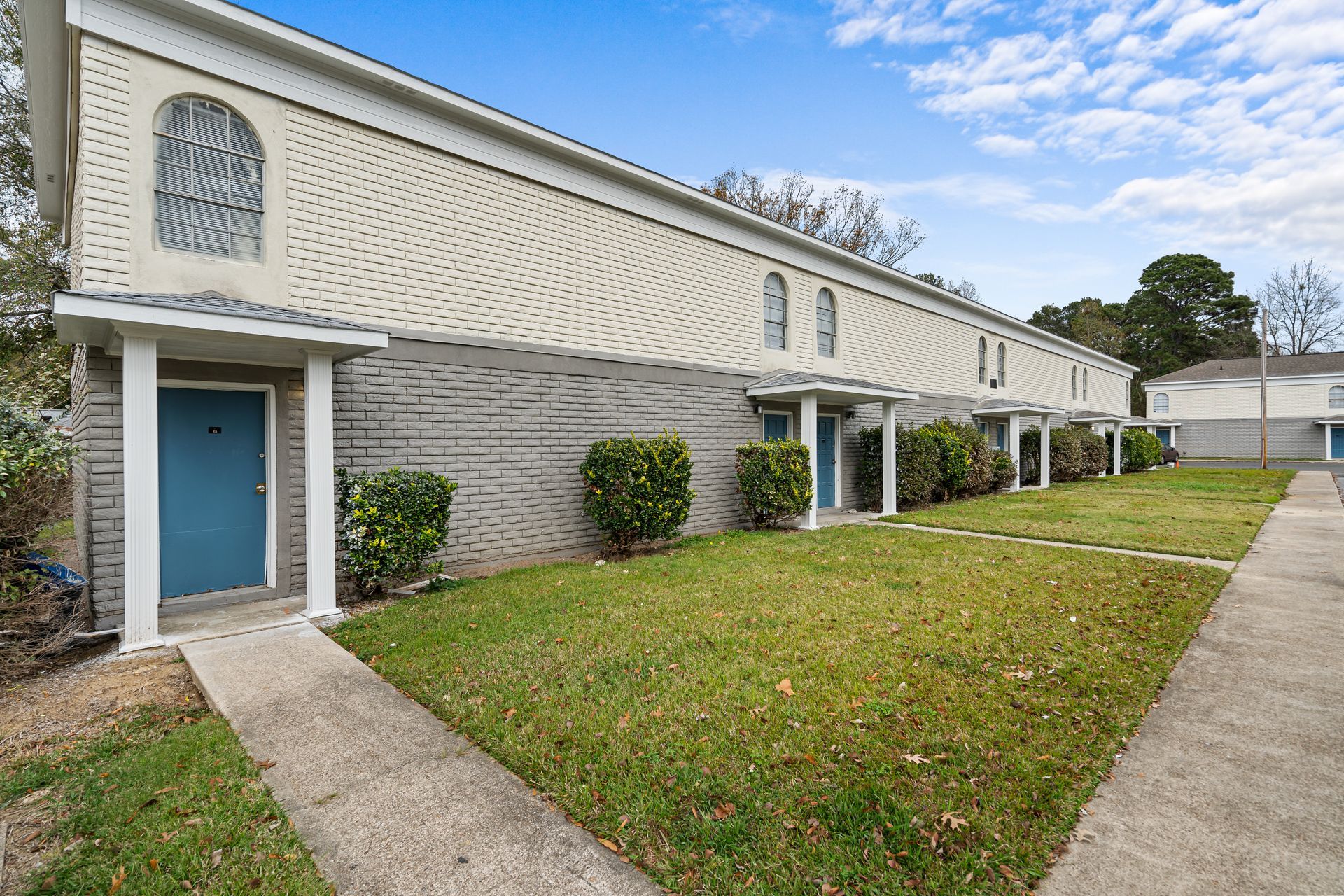 Apartment building with blue doors, white brick exterior, and a grassy courtyard under a blue sky