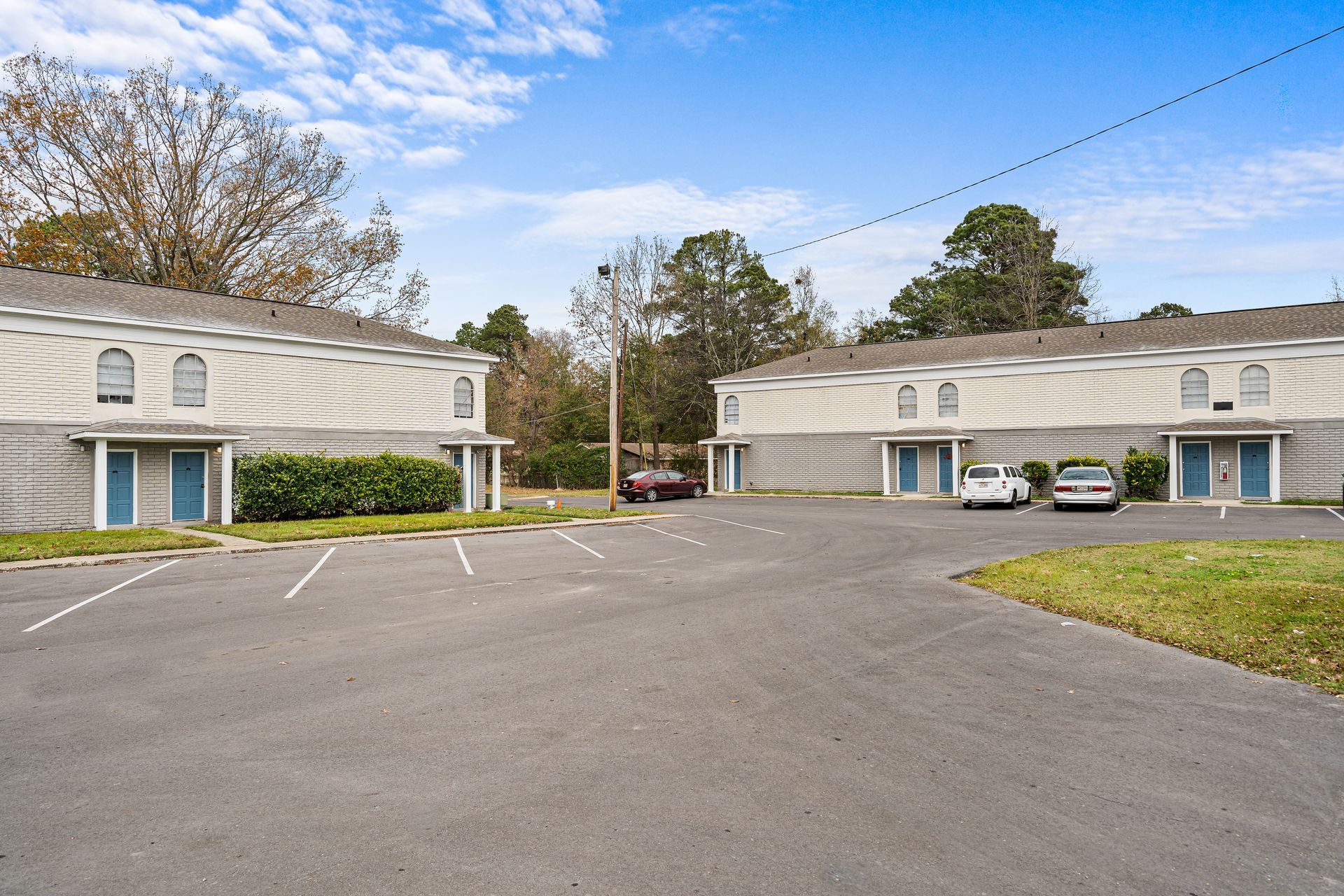 Two beige apartment buildings with a large empty parking lot under a blue sky