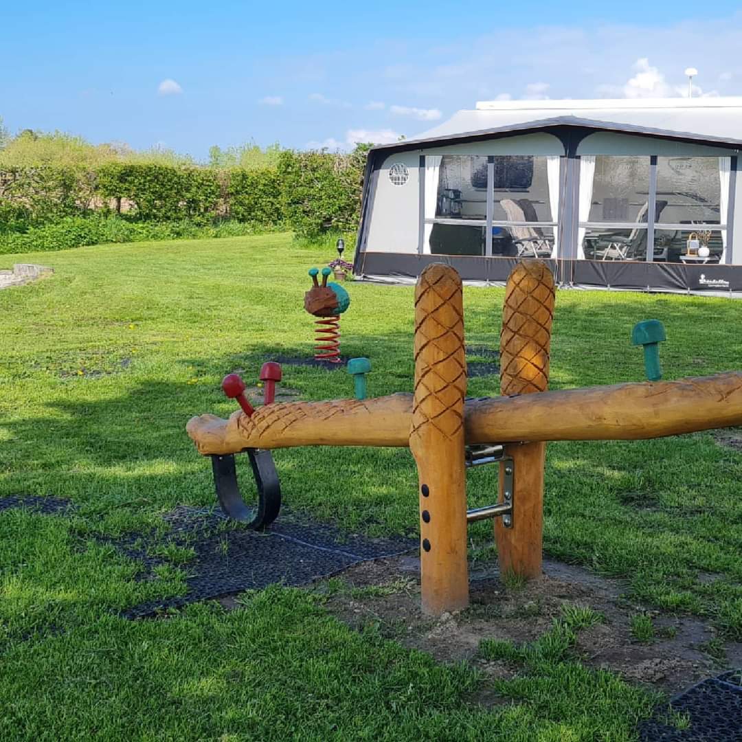 Balancebomme af træ på naturlegeplads med fortelt i baggrunden.