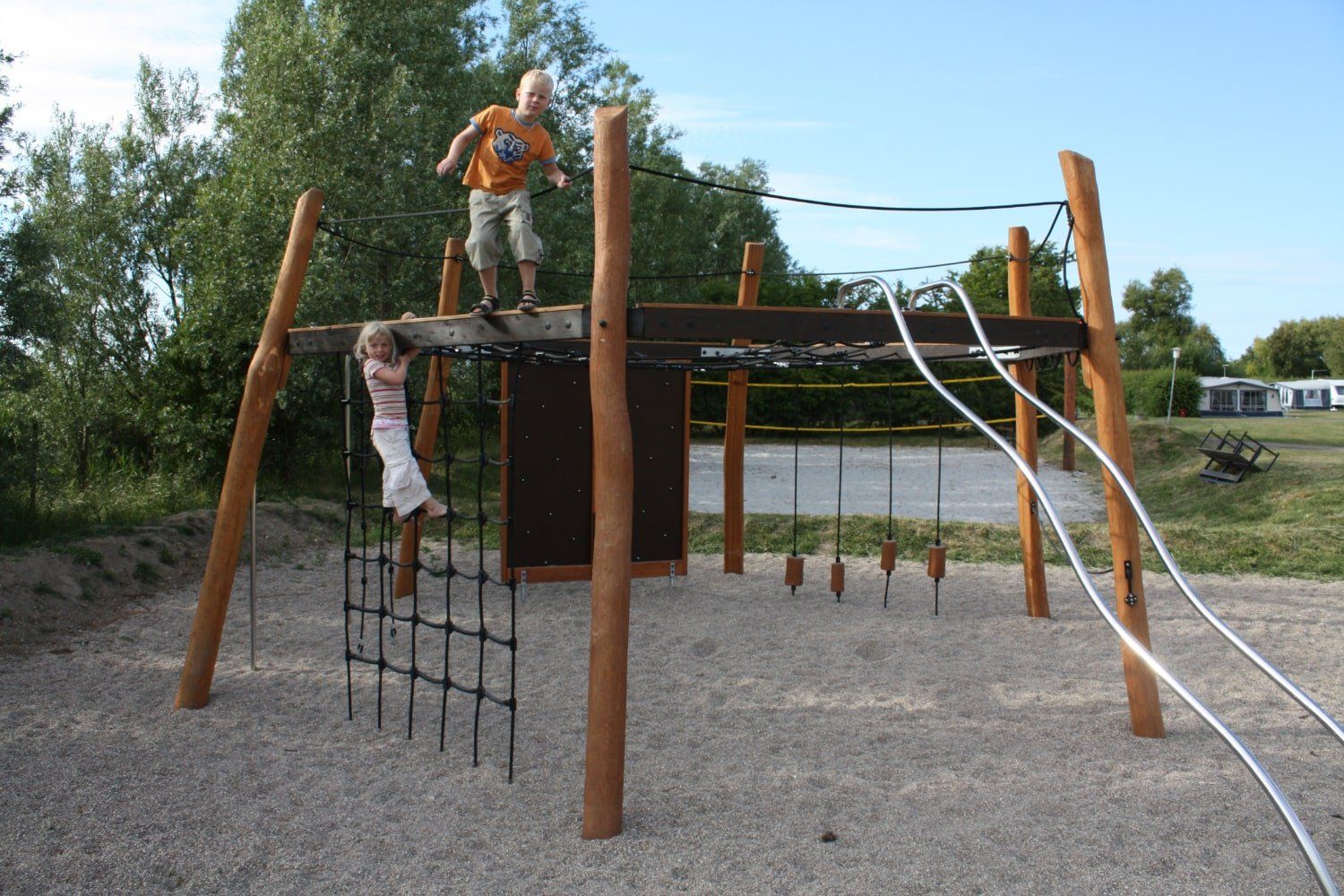 Børn leger på stort klatrestativ af træ med net på naturlegepladsen.