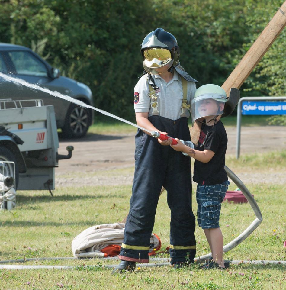 Børn leger brandmænd og sprøjter med vandslange på campingpladsen.