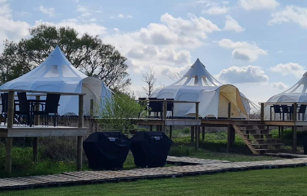 Mooie glamping-tent op een houten terras met barbecue.
