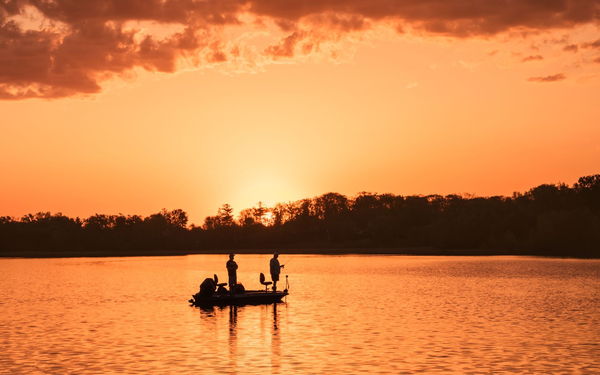 Two people are fishing in a boat on a lake at sunset.