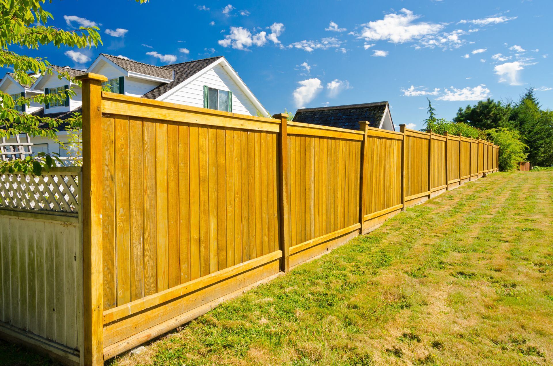 A wooden fence surrounds a lush green field in front of a house.