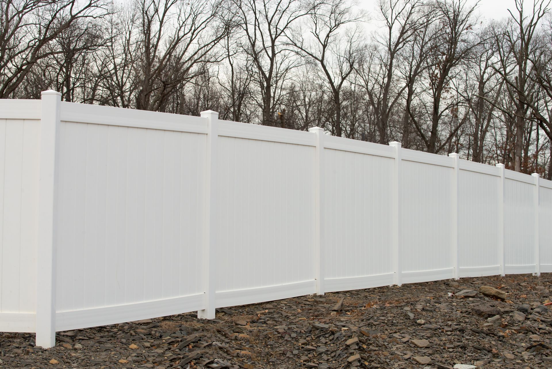 A white fence surrounds a dirt field with trees in the background.