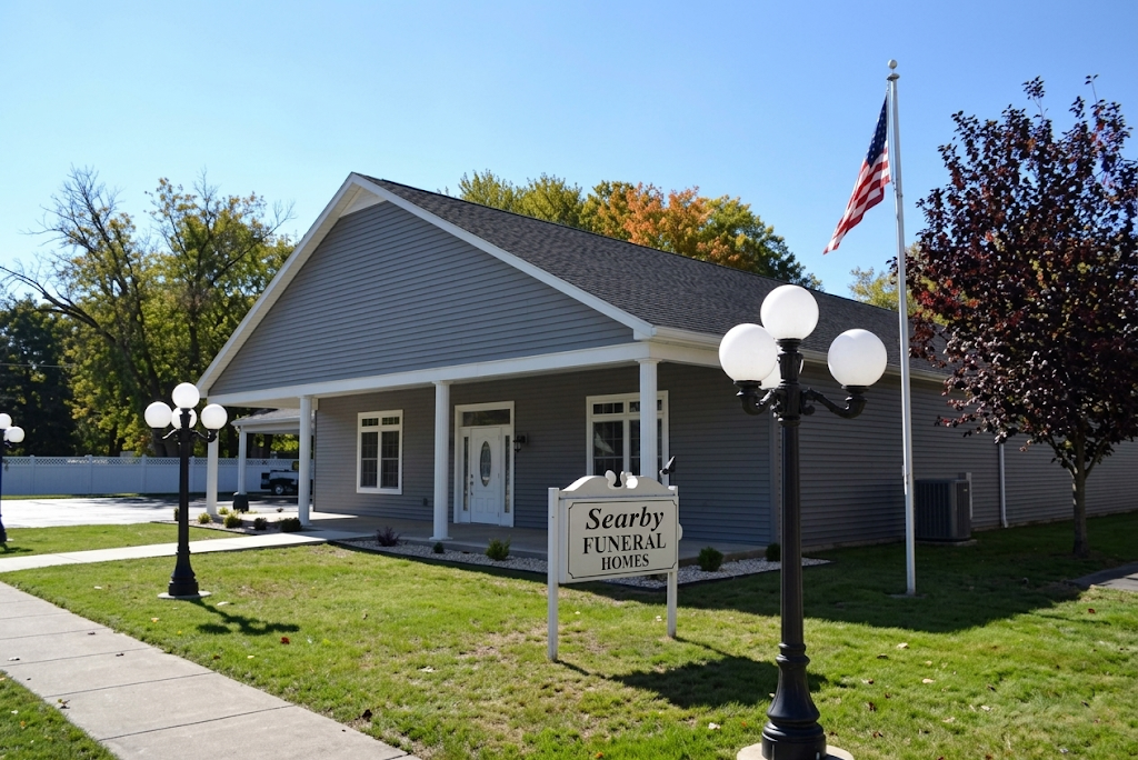 Gray funeral home with white trim, black lampposts, an American flag, and a sign by the sidewalk.