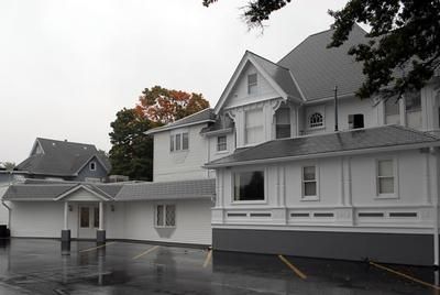 Large white house with gray roof and wet driveway on a rainy day