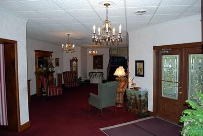 Elegant lobby with chandeliers, red carpet, chairs, tables, and glass doors opening outside