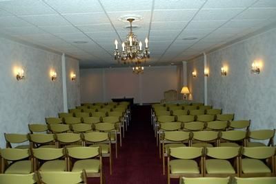 Empty conference room with rows of green chairs, red carpet, and a chandelier ceiling light