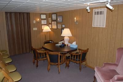 Small waiting room with round table, lamps, framed certificates, beige walls, and pink chairs