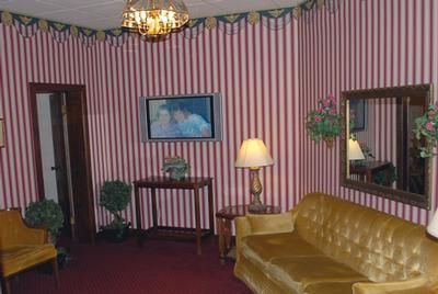 Elegant hotel lobby with chandeliers, red carpet, striped armchairs, and a lamp.