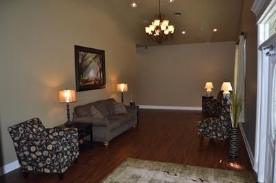 Living room with gray sofa, patterned chairs, lamps, hardwood floor, and a chandelier.
