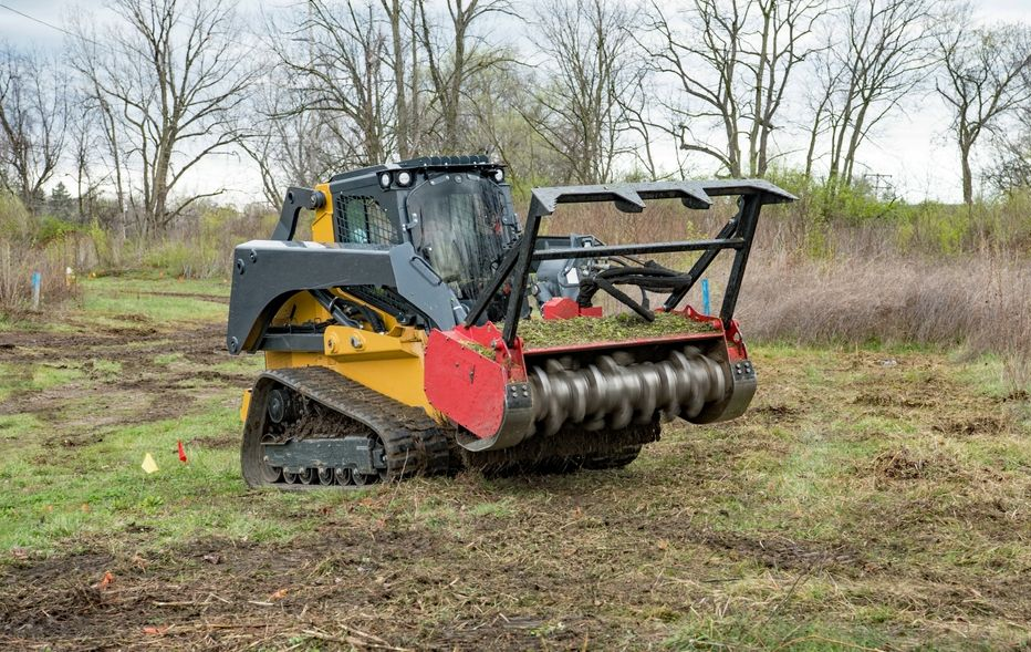 Yellow and black skid steer with rotary cutter clearing brush in a field.