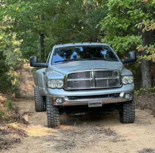 A man is driving a truck on a dirt road with a trailer on the back