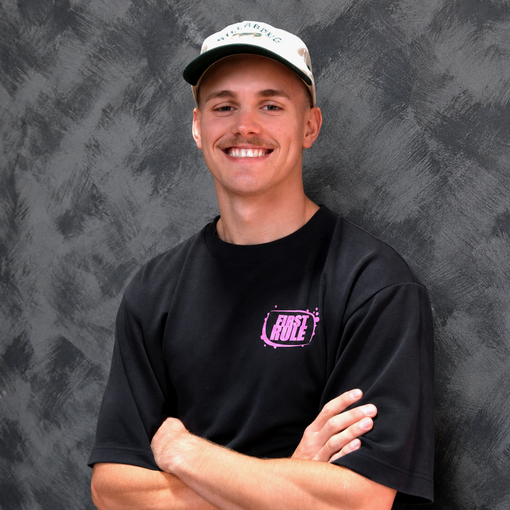 Smiling person in a black shirt and cap with arms crossed against a gray backdrop
