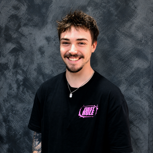 Smiling person in a black T-shirt standing before a gray textured backdrop