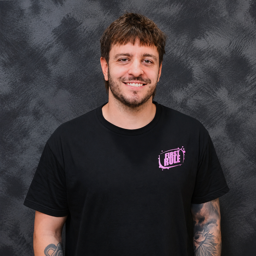 Smiling person in a black T-shirt with pink logo, standing against a gray backdrop