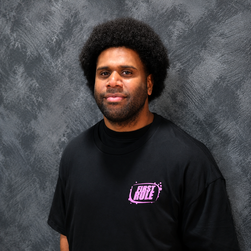 Person in a black shirt with a pink logo, standing against a gray textured backdrop