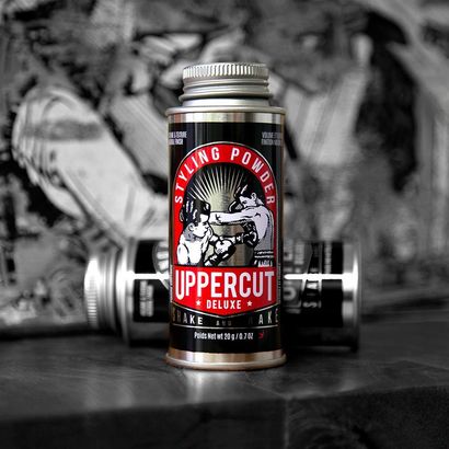 Black and red Uppercut Deluxe matte clay tin on a barbell, with blurred gym gear in the background