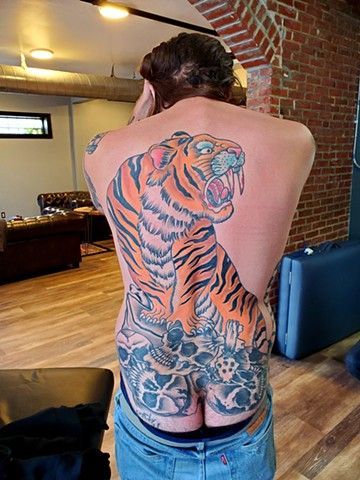 A man with a tiger tattoo on his back is standing in a living room.