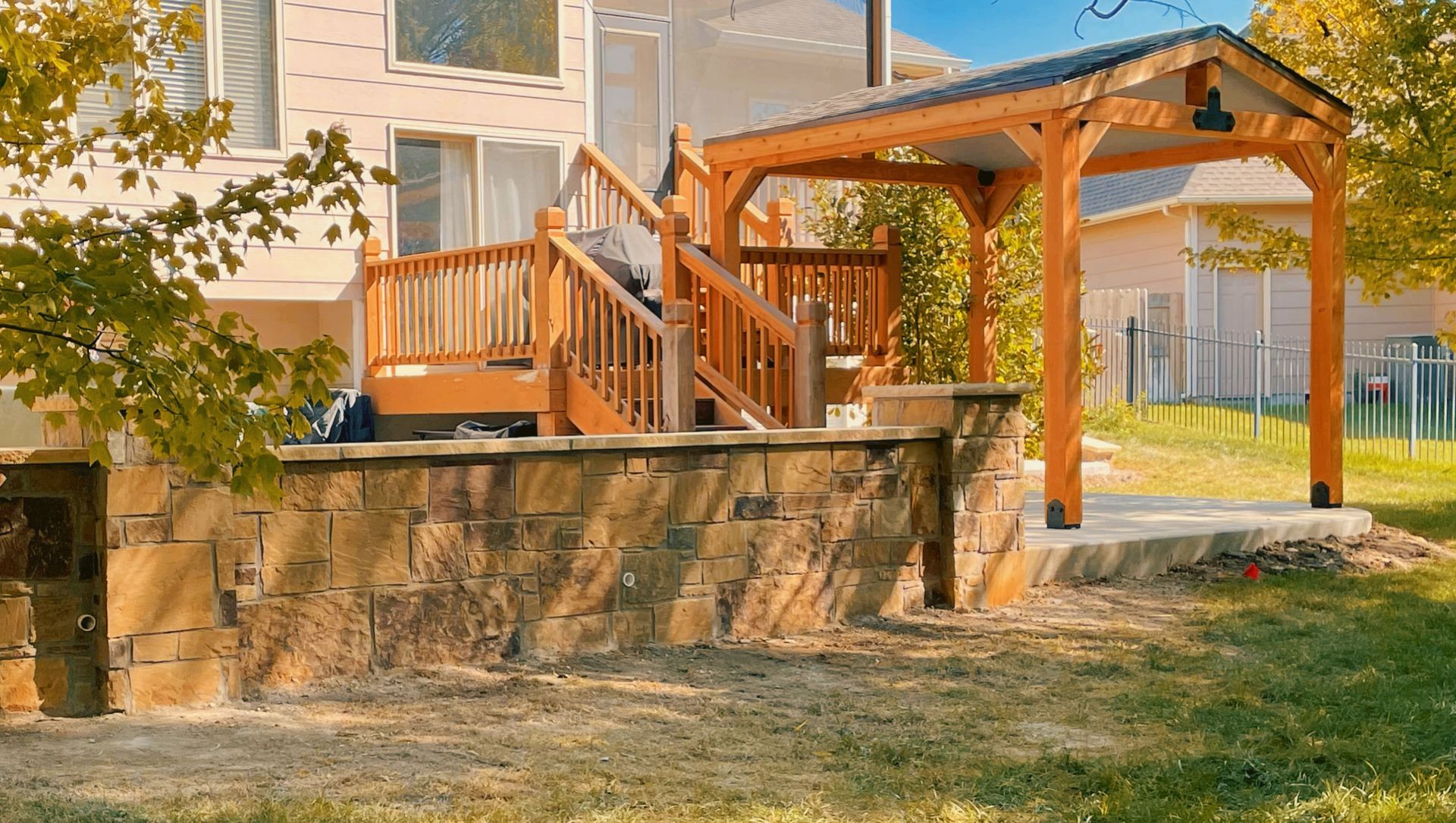 A wooden deck with stairs and a stone wall in front of a house.
