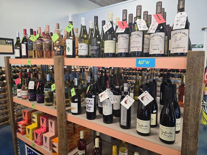 Wine bottles displayed on wooden shelves in a store aisle with price tags.
