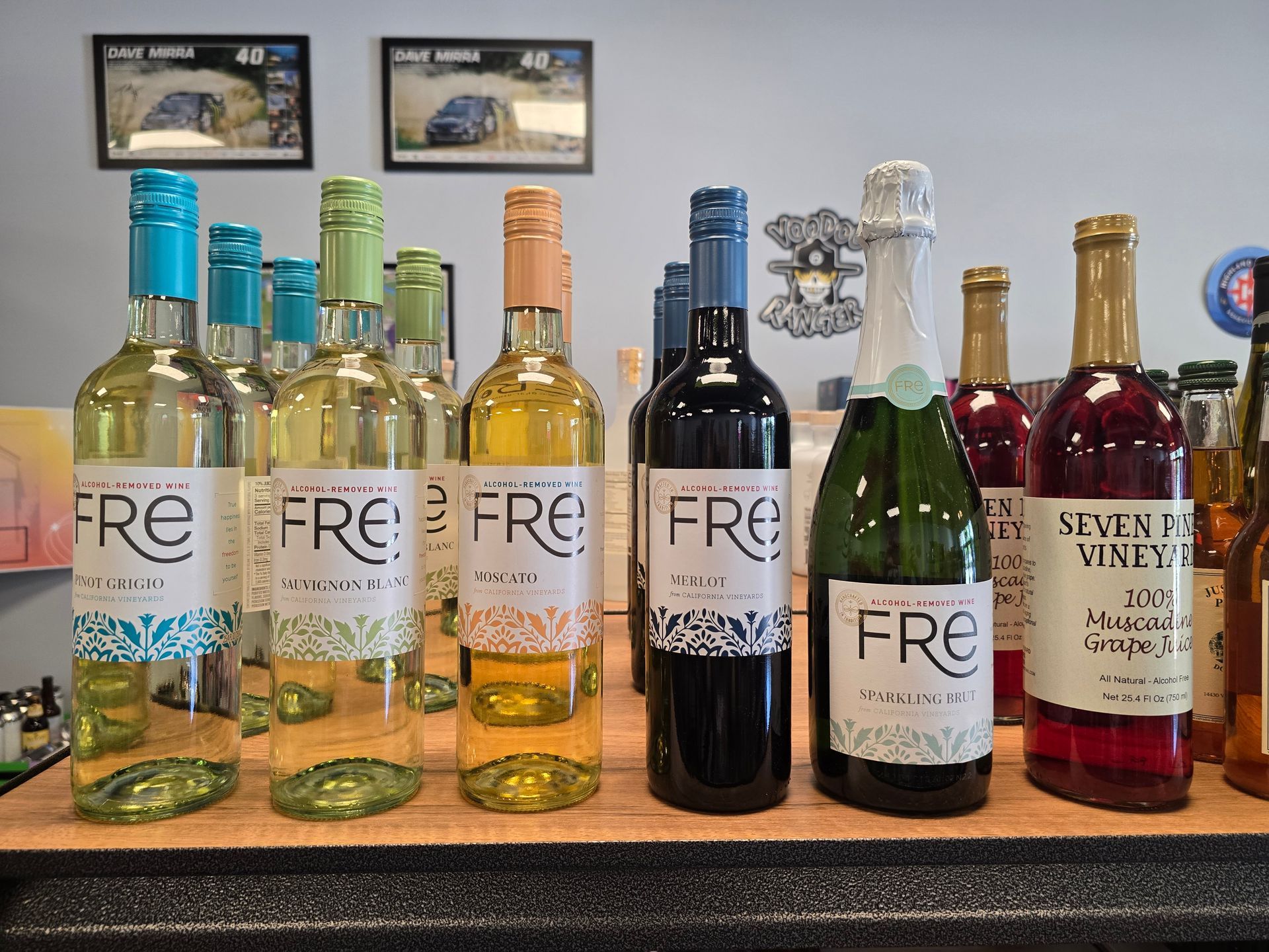 Assorted wine and sparkling bottles lined up on a shelf, including several labeled “FRÉ.”