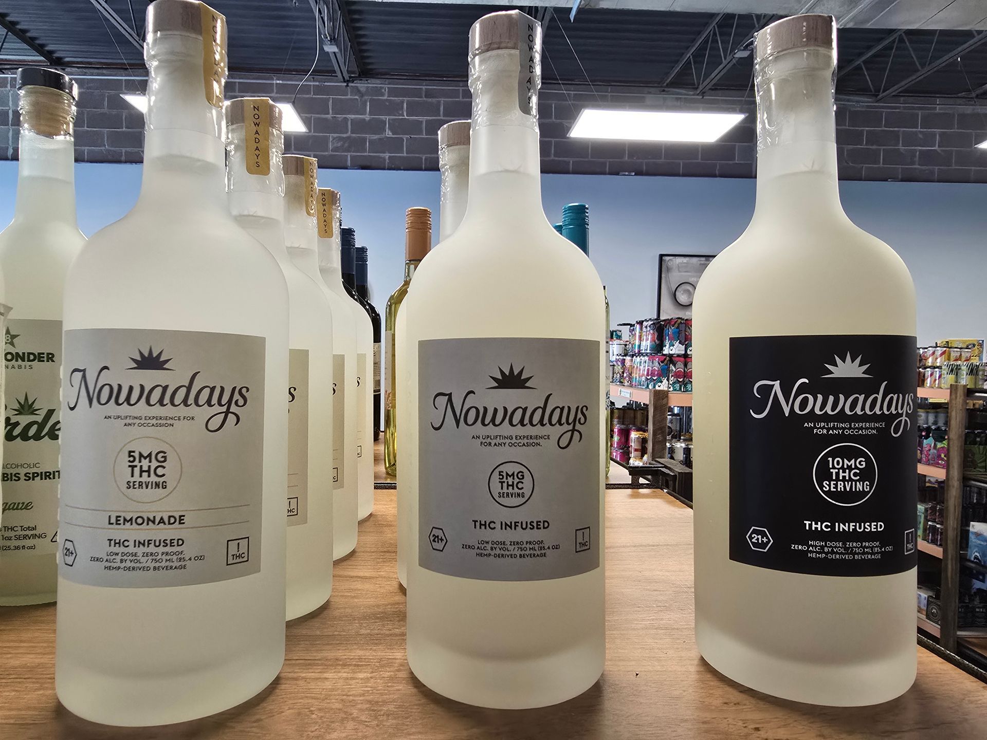 Three frosted “Nowadays” liquor bottles on a store shelf, including two white labels and one black label.