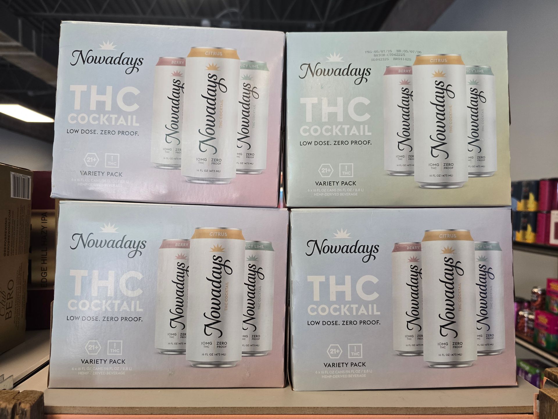 Display of four boxed THC cocktail six-packs in pink and beige packaging on a shelf