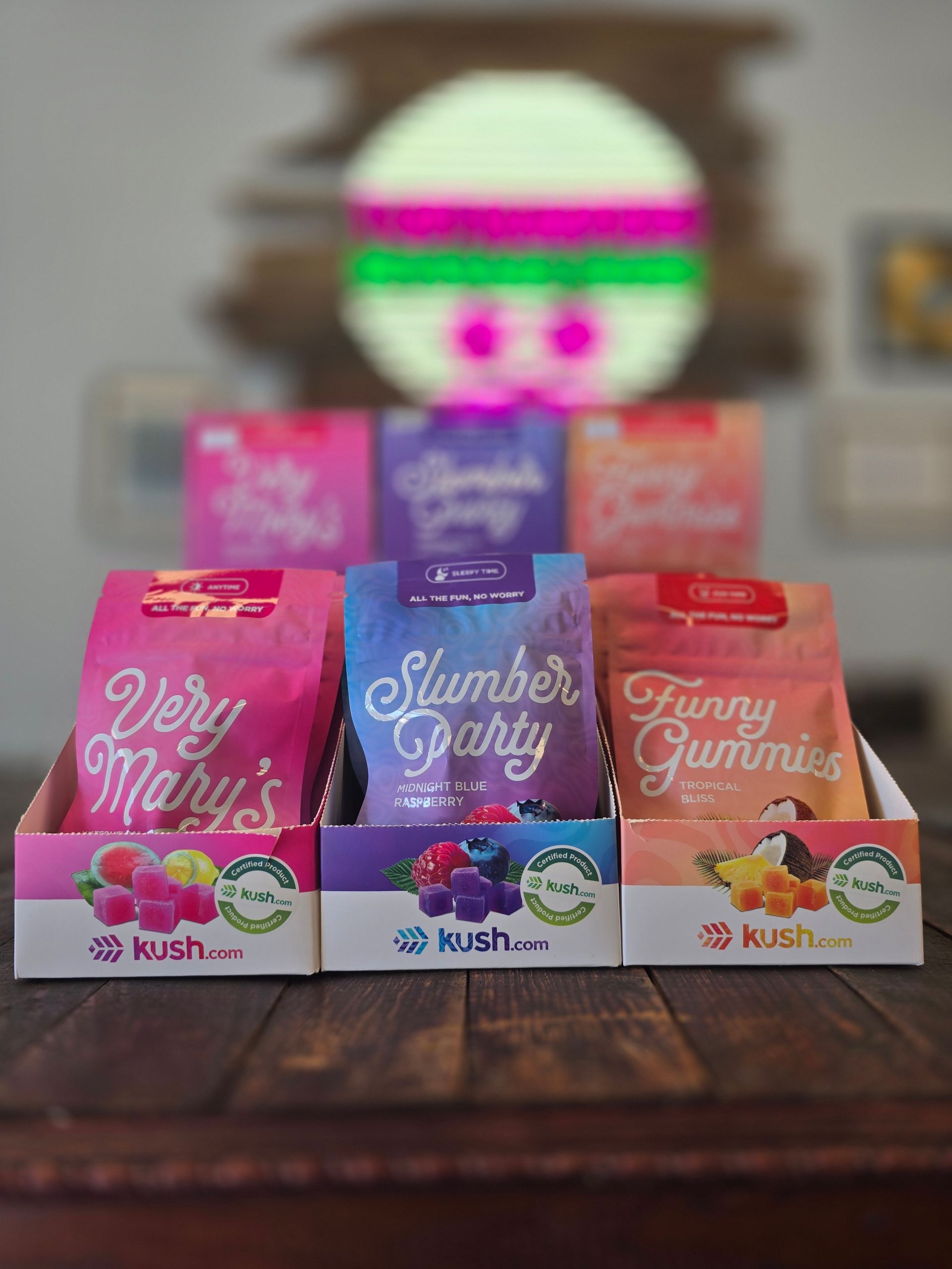 Three colorful candy boxes on a wooden table with a blurred decorative figure in the background