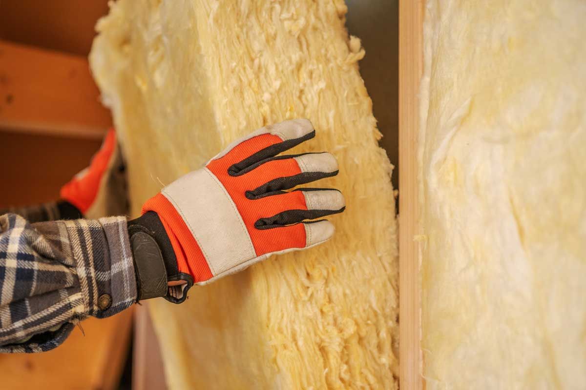 Behandsket håndpressning af gul glasfiberisolering mellem vægstolper