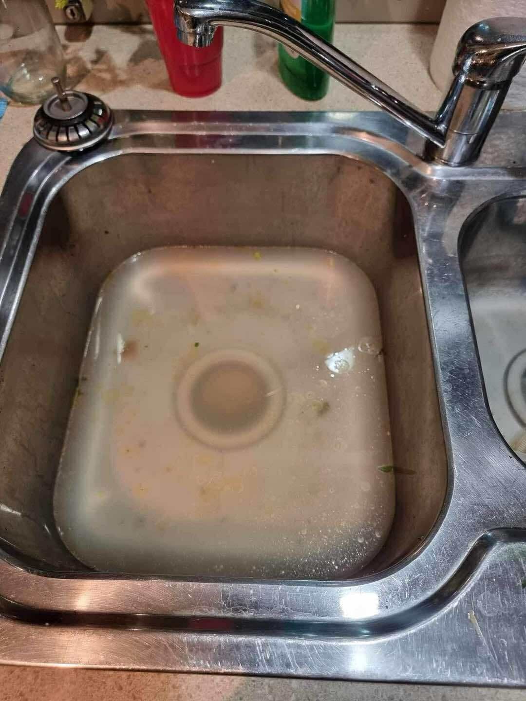 A person washing their hands under a stream of water in a modern dark grey kitchen sink.