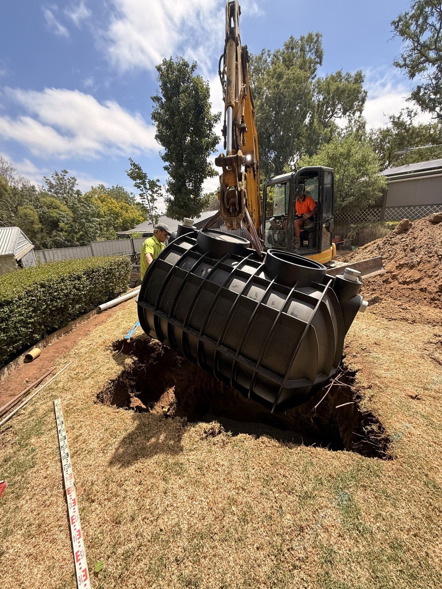 A green, corrugated suction hose runs into an open, round septic tank hole next to a heavy metal manhole cover.