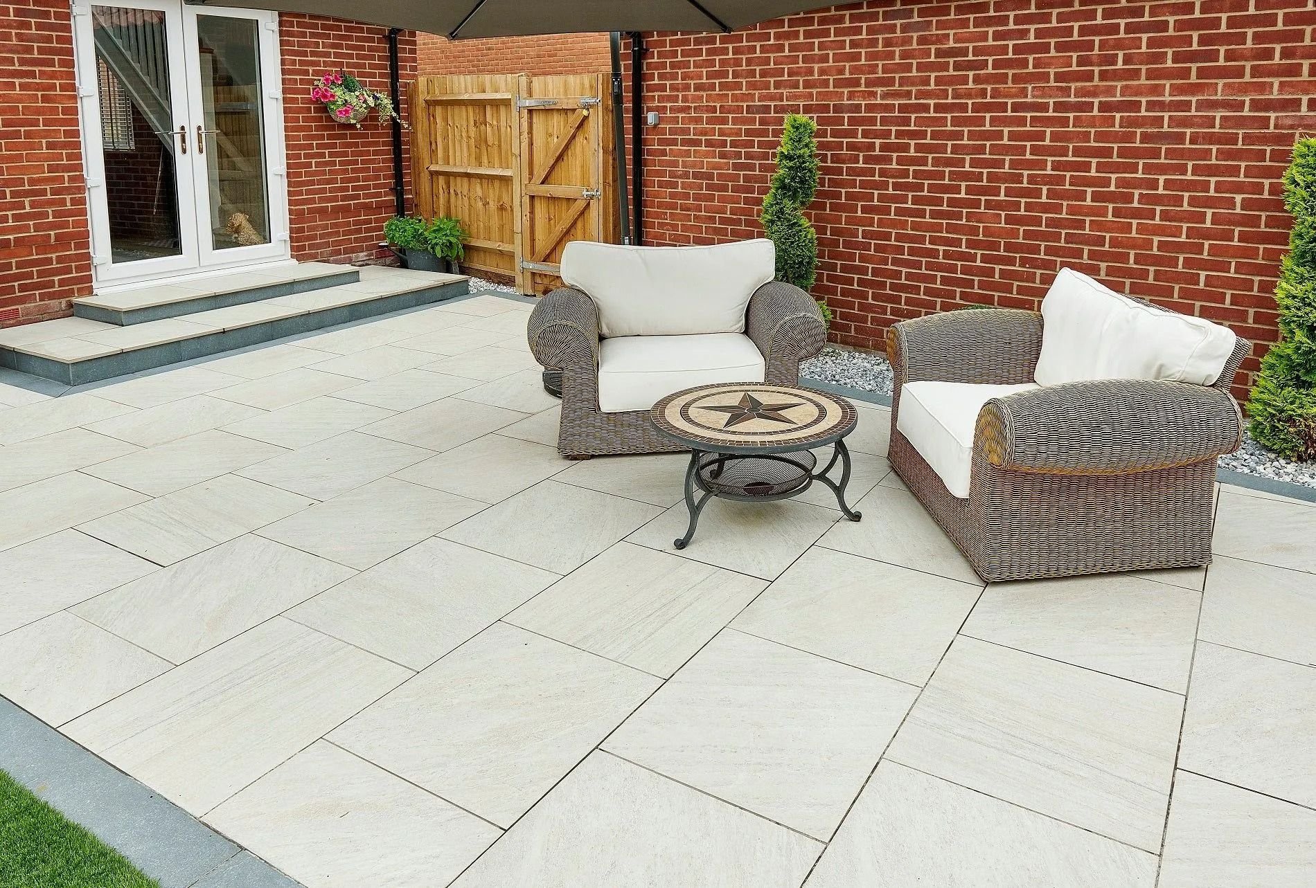 Brick patio with wicker chairs and small table beside a brick house and wooden gate.