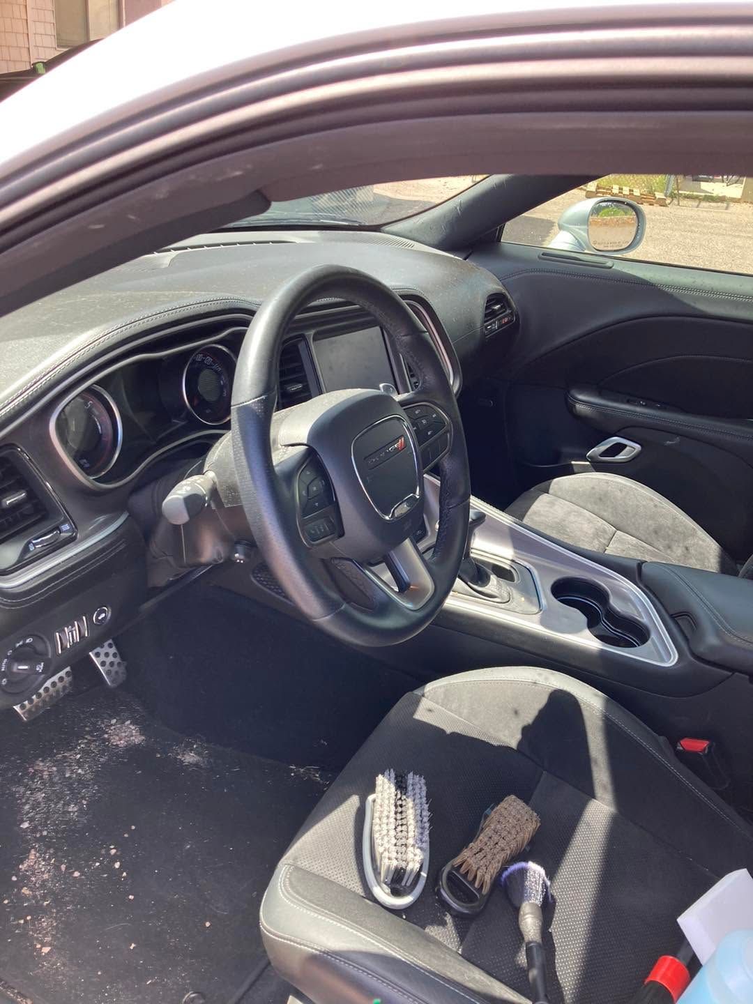 Driver’s seat interior of a car with black dashboard and steering wheel, sunlit door open.