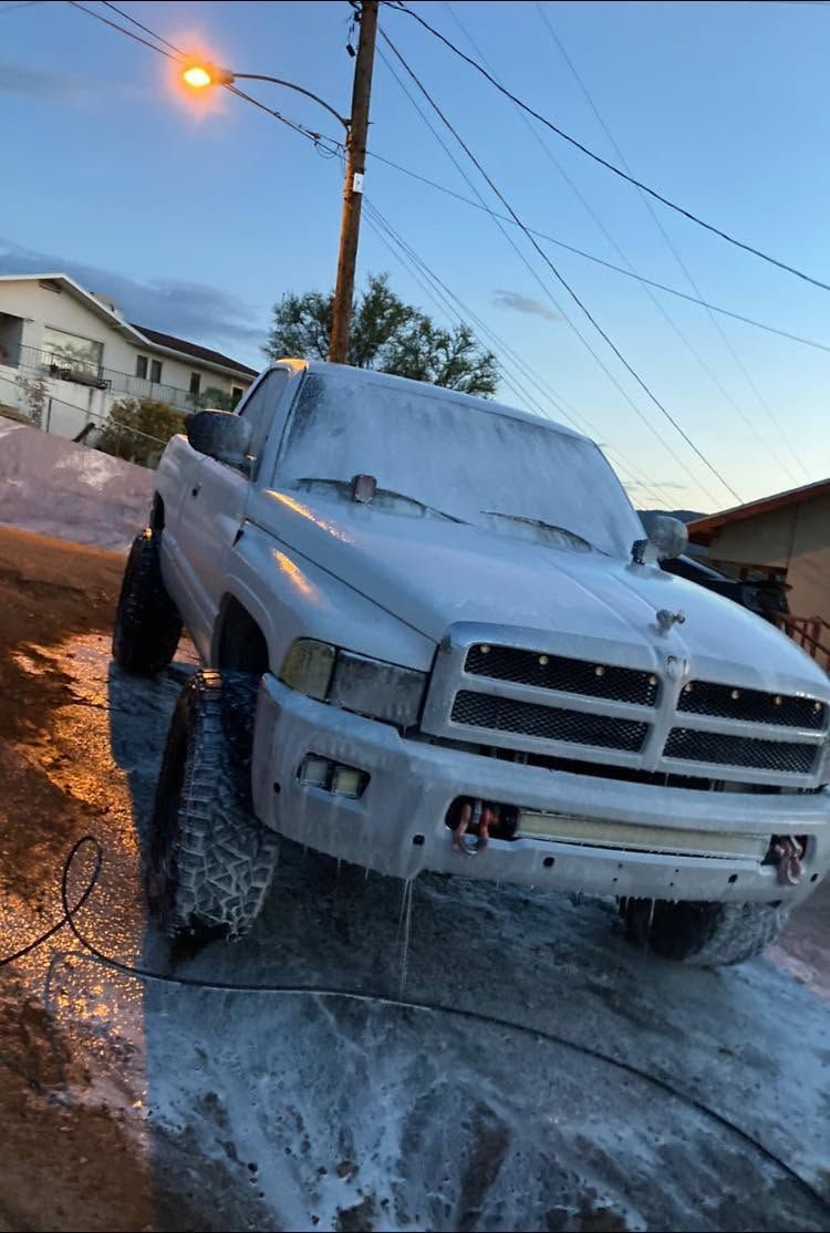 White truck covered in soap suds on a sloped driveway at sunset, with water and foam on the ground.